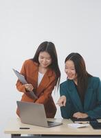 Two young Asian businesswoman discuss investment project working and planning strategy. Business people talking together with laptop computer at office. photo