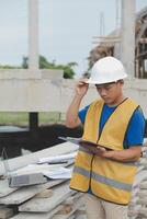 Asian man architect holds blueprint with skyscraper background, Asian male architect builder engineer design working planning confident outdoors in construction site. photo