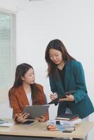 Two young Asian businesswoman discuss investment project working and planning strategy. Business people talking together with laptop computer at office. photo