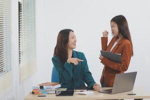 Two young Asian businesswoman discuss investment project working and planning strategy. Business people talking together with laptop computer at office. photo