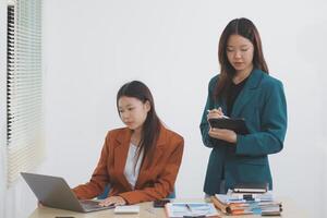Two young Asian businesswoman discuss investment project working and planning strategy. Business people talking together with laptop computer at office. photo