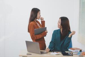 Two young Asian businesswoman discuss investment project working and planning strategy. Business people talking together with laptop computer at office. photo