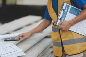 Young handsome asian civil engineer holding tablet looking forward and thinking, planning on construction building background. Evolution construction concept. photo