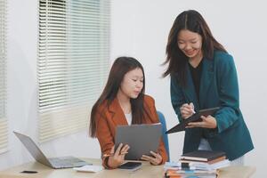 Two young Asian businesswoman discuss investment project working and planning strategy. Business people talking together with laptop computer at office. photo