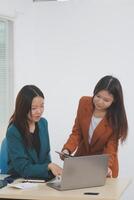 Two young Asian businesswoman discuss investment project working and planning strategy. Business people talking together with laptop computer at office. photo