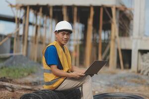 Asian man architect holds blueprint with skyscraper background, Asian male architect builder engineer design working planning confident outdoors in construction site. photo