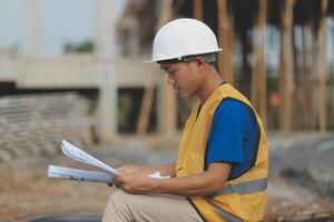 Asian man architect holds blueprint with skyscraper background, Asian male architect builder engineer design working planning confident outdoors in construction site. photo