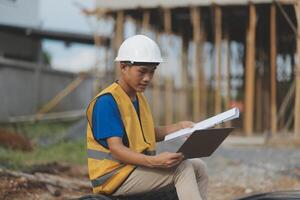Asian man architect holds blueprint with skyscraper background, Asian male architect builder engineer design working planning confident outdoors in construction site. photo