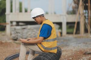 Asian man architect holds blueprint with skyscraper background, Asian male architect builder engineer design working planning confident outdoors in construction site. photo