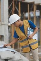 Young handsome asian civil engineer holding tablet looking forward and thinking, planning on construction building background. Evolution construction concept. photo