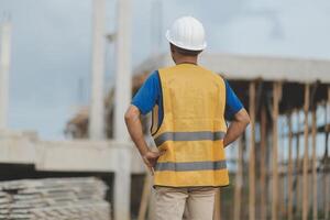 Asian man architect holds blueprint with skyscraper background, Asian male architect builder engineer design working planning confident outdoors in construction site. photo