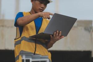 Young handsome asian civil engineer holding tablet looking forward and thinking, planning on construction building background. Evolution construction concept. photo
