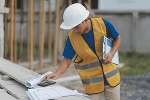 Young handsome asian civil engineer holding tablet looking forward and thinking, planning on construction building background. Evolution construction concept. photo