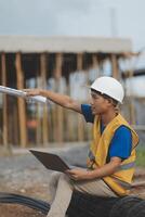 Asian man architect holds blueprint with skyscraper background, Asian male architect builder engineer design working planning confident outdoors in construction site. photo