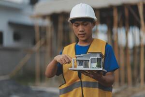 Young handsome asian civil engineer holding tablet looking forward and thinking, planning on construction building background. Evolution construction concept. photo