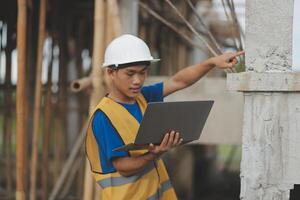 Young handsome asian civil engineer holding tablet looking forward and thinking, planning on construction building background. Evolution construction concept. photo