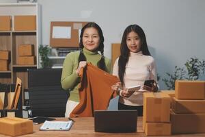 Startup SME small business entrepreneur of freelance Asian woman wearing apron using laptop and box to receive and review orders online to prepare to pack sell to customers, online sme business ideas. photo