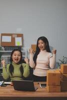 Startup SME small business entrepreneur of freelance Asian woman wearing apron using laptop and box to receive and review orders online to prepare to pack sell to customers, online sme business ideas. photo