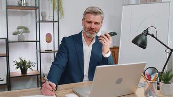 Mature business man working, having mobile phone talk at office workplace using messenger chat apps video