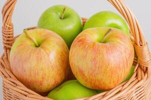 Two different varieties of apples in a wicker basket on a gray background. Fruits, apples. photo