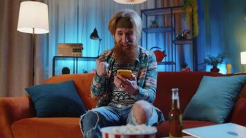 Handsome hippie man at home use smartphone typing browsing wow yes found out great big win celebrate video