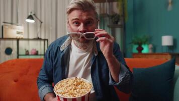 Man sitting on couch eating popcorn and watching interesting TV serial, sport game online at home video