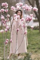 Woman magnolia flowers, surrounded by blossoming trees., hair down, white hat, wearing a light coat. Captured during spring, showcasing natural beauty and seasonal change. photo