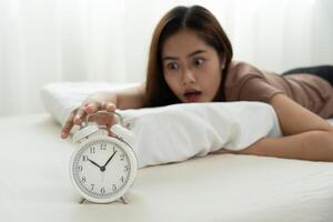 Shocked Asia young woman looking at clock alarm, lady is late appointment or work or class study, overslept, difficulty get up in mornings, time worried, not on time, sleepy, over due, Hurry up time photo