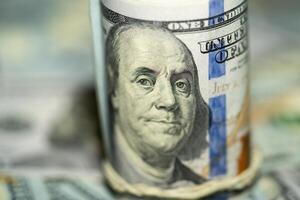 Close-up of rolled hundred dollar bill on top of cash photo