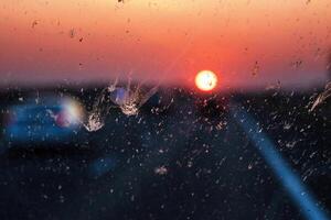 Blurry highway through a smudged dirty car windshield, affecting visibility during orange sunset, emphasizing traffic safety concerns and the importance of clean glass for safe travel. photo