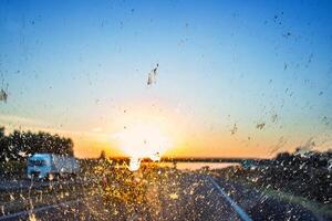 Blurry highway through a smudged dirty car windshield, affecting visibility during sunset, emphasizing highway traffic safety concerns and the importance of clean glass for safe travel. photo