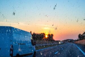 Sunset view through a dirty car windshield on the highway with a van in motion, focusing on travel, visibility, and road safety concerns. Transportation, logistics, road traffic. Copy space photo