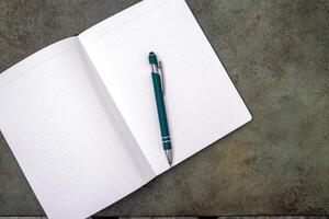 An open notebook with a pen lies on a dark textured surface. photo