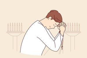 Man prays while standing in church near candlesticks, holds christian crucifix and closes eyes vector