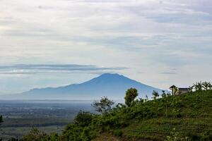 Beautiful view of misty Mount Lawu from distance, a massive compound stratovolcano straddling the border between Ngawi, East Java and Central Java, Indonesia photo