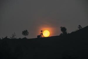 Silhouette of a hill and hut with the sun shining softly in the background. A serene atmosphere in the mountains in the morning. photo