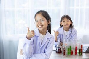 Two young asian students in scientific lab gown while studying science lesson in the classroom for education, literacy and tutoring concept with copy space photo