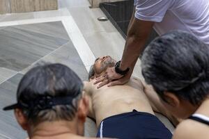 Life guard is performing CPR to the drowning asian senior man at sport club with the family support for accident and emergency medical procedure service and life insurance photo