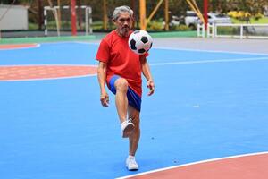 Senior Asian man in retirement age playing soccer football at outdoor court for healthy and fun activity to exercise and workout against aging illness photo