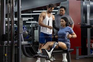 Asian woman with prosthetic leg from amputation from doing weight training workout exercise using machine at gym with professional trainer for handicap and disability people and recovery photo