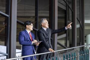 Asian senior businessman giving advice to the new manager while working inside modern style office photo