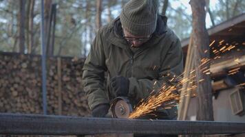 A skilled worker is focused on shaping metal with a grinding tool, creating sparks in a wooded area. The scene captures the creative process in natural light. video
