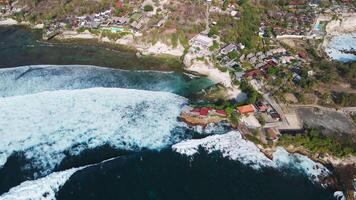 Scenic coastline with resorts and hotels, and breaking ocean waves on Nusa Ceningan, drone view video