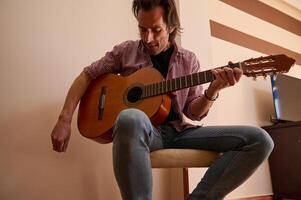 Man playing classical acoustic guitar while sitting indoors tuning strings photo