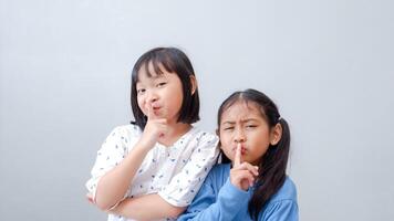two pretty cheerful preteen girls on grey background, holding fingers on lips. Symbol of hush gesture of asking to be quiet. photo