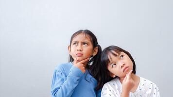 Thoughtful two Asian little girl child touch chin with finger thinking or considering, pensive lovely friend making decision imagining idea posing. photo