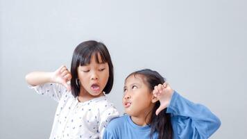 Young girl teasing and mocking a friend - sticking her tongue out, isolated on gray background. photo