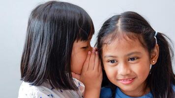 Two girls telling a secret and expressing surprise isolated on grey. photo
