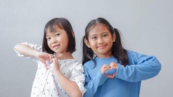 Cute little children with hearts fingers sign on grey background. Friendship concept. photo