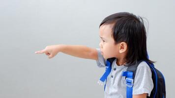 Cute Asian child student with backpack pointing with finger, confident gesture looking serious and mad photo